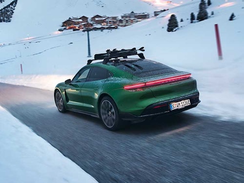 Green Porsche Taycan driving on snowy mountain road towards town