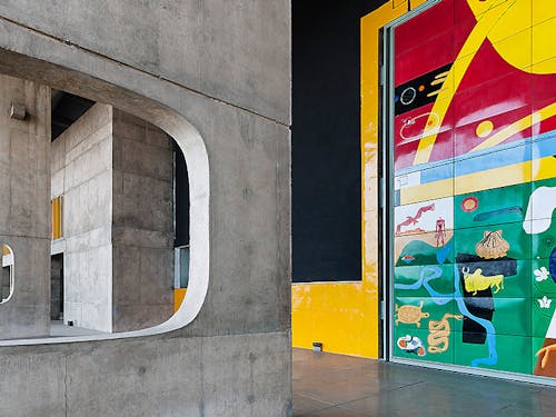 Exposed concrete building with bright, expressive modern wall art 