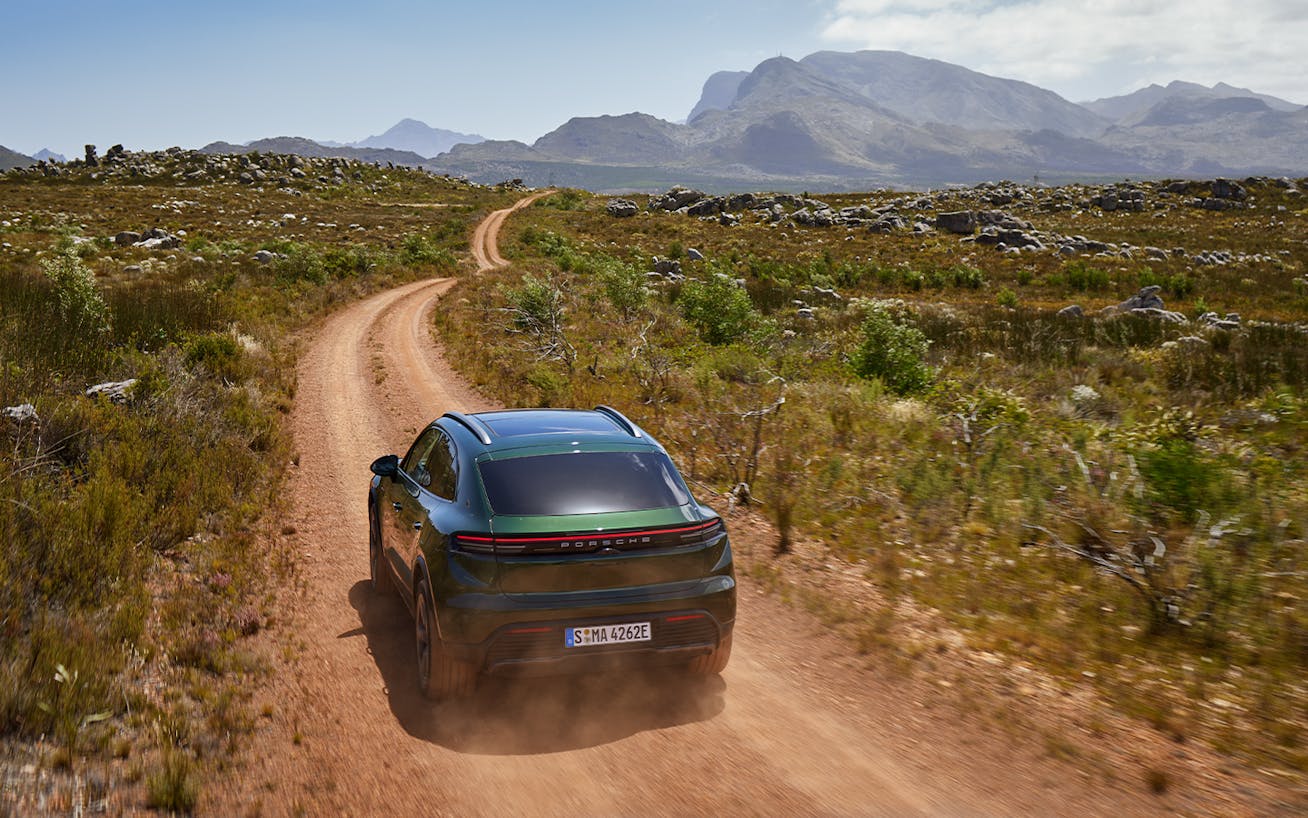 Porsche Macan 4S Electric on dirt road, hills in background