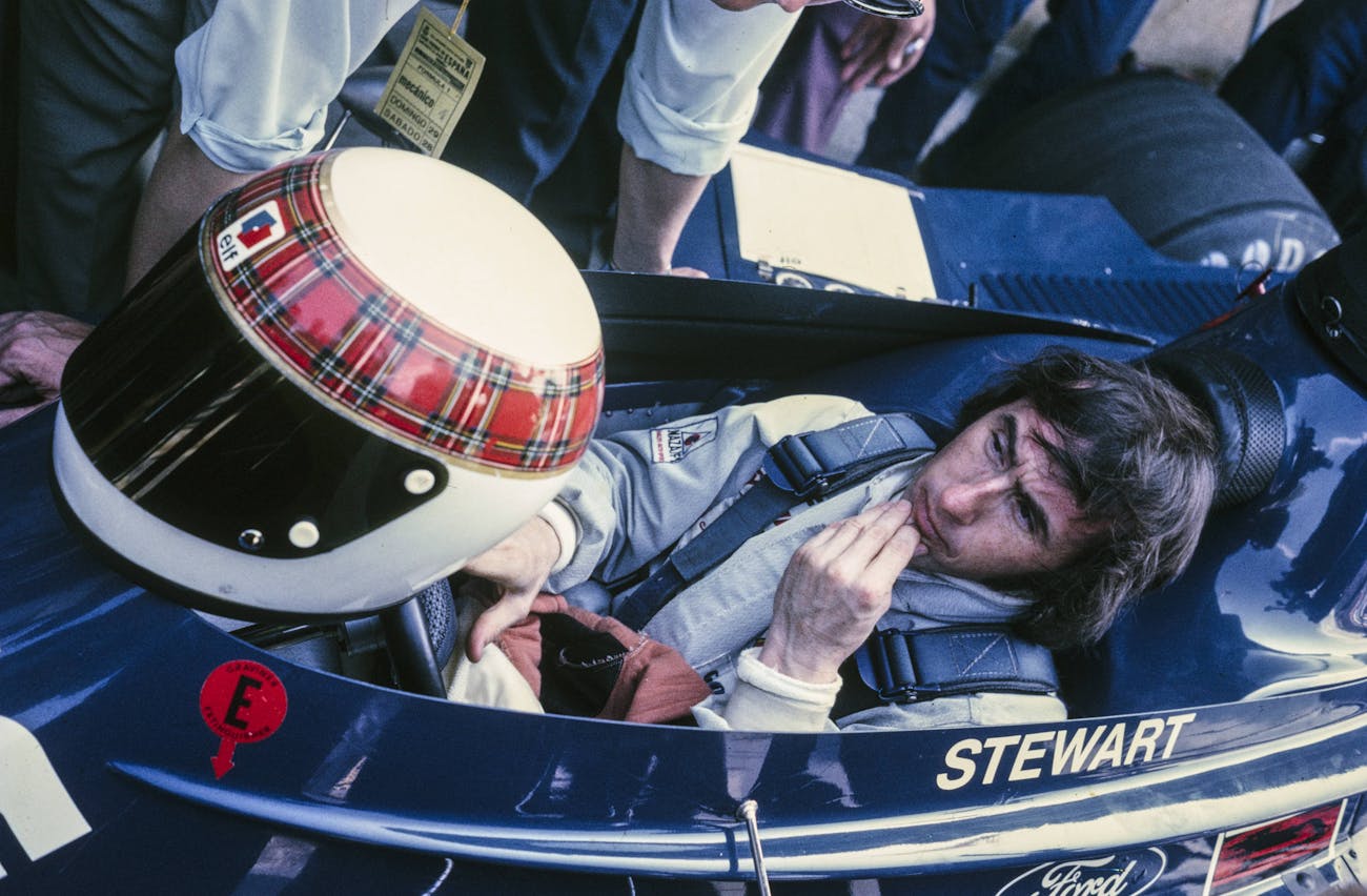 Jackie Stewart in racecar, tartan helmet in front of him