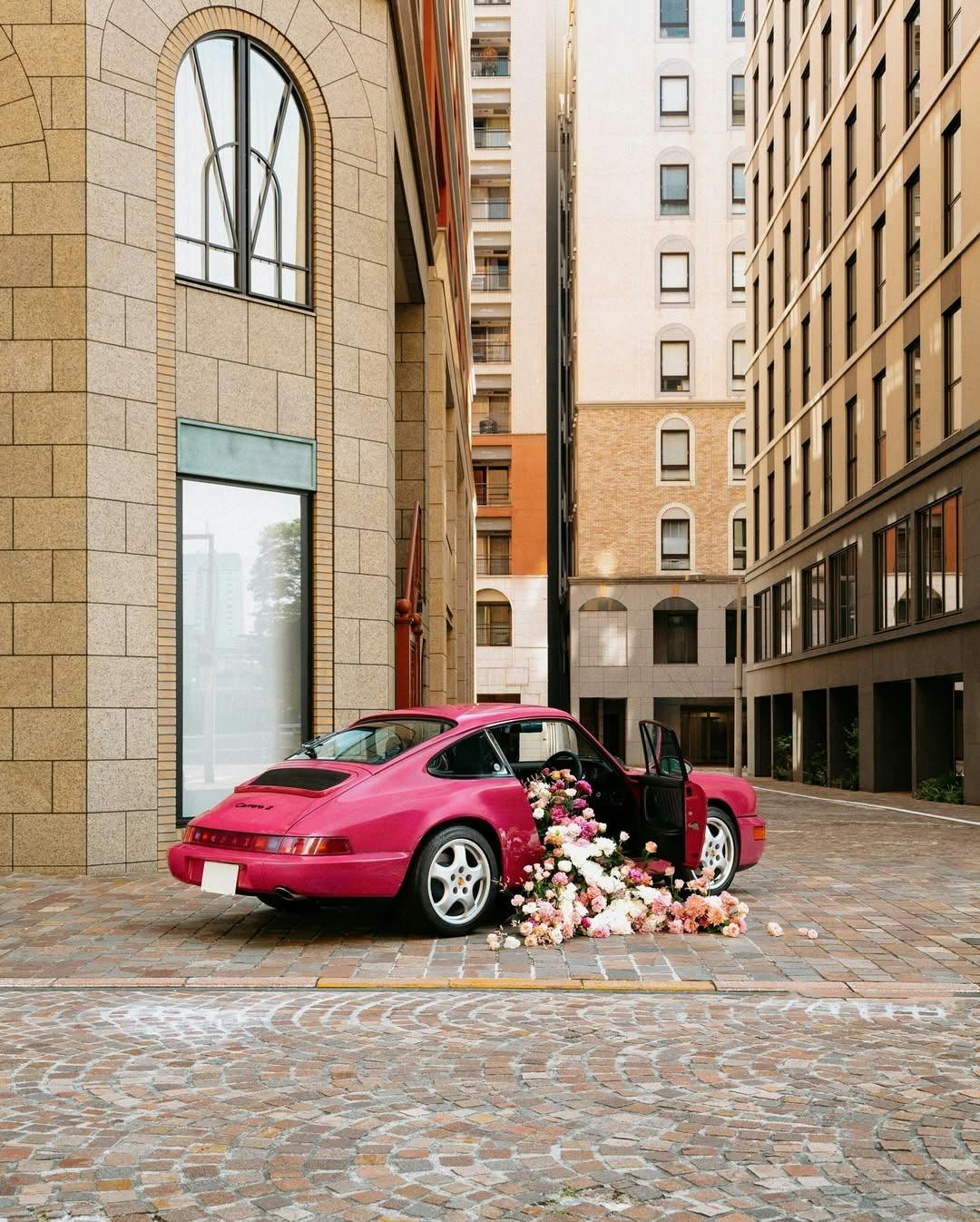 Image of a classic Porsche 911 parked on a city street with the door open and flowers spilling out