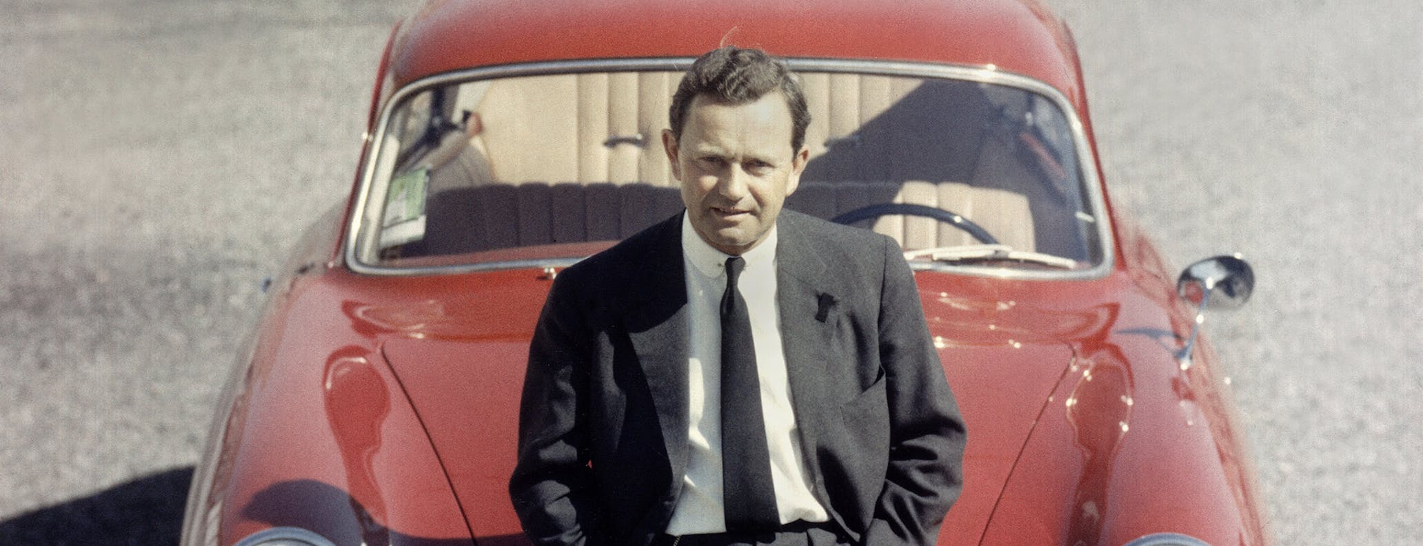 Ferry Porsche is leaning against the front of a red Porsche 356 “No 1” Roadster.