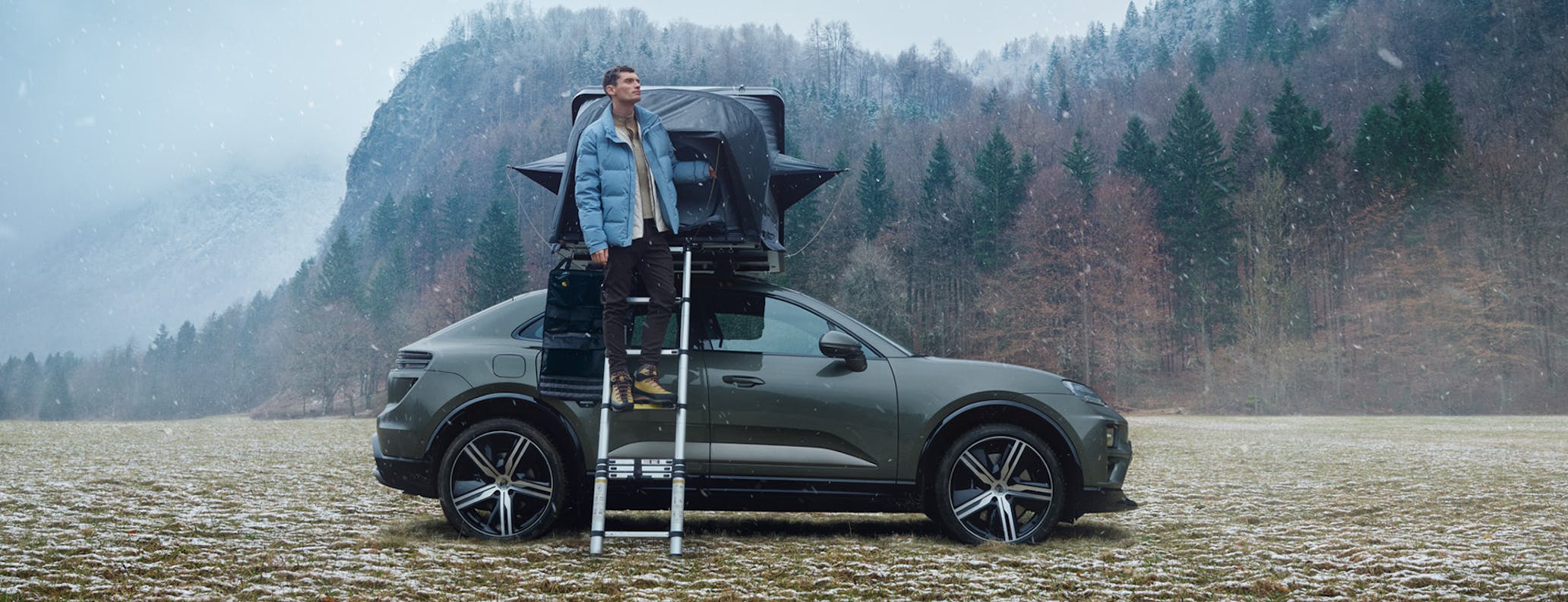 Man on ladder with grey Porsche Macan with roof tent