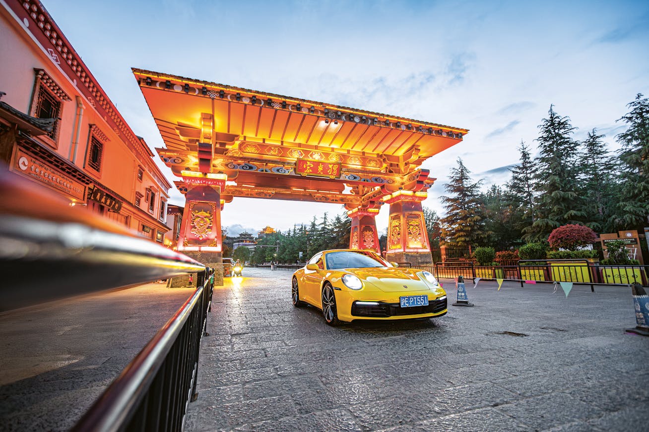 Yellow Porsche 911 Carrera in Lijang, China in front of traditional Chinese archway