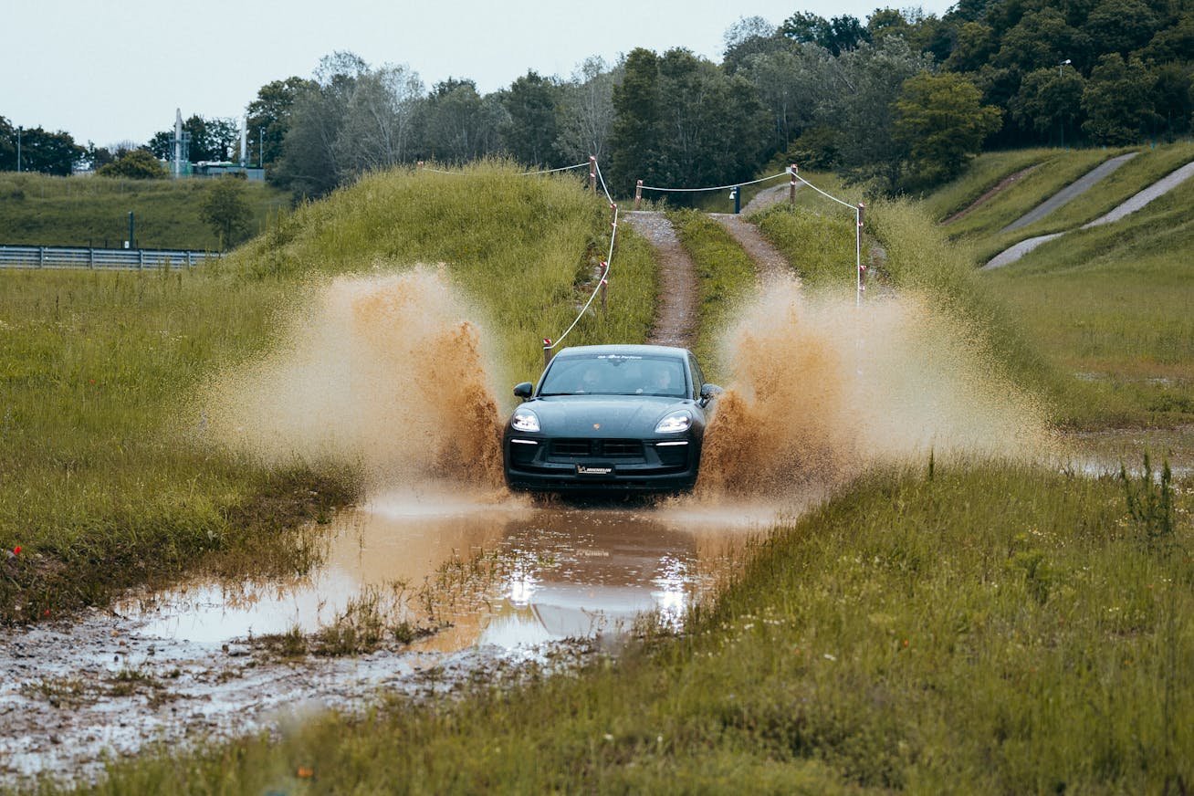 Porsche Cayenne drives down a muddy road into a puddle