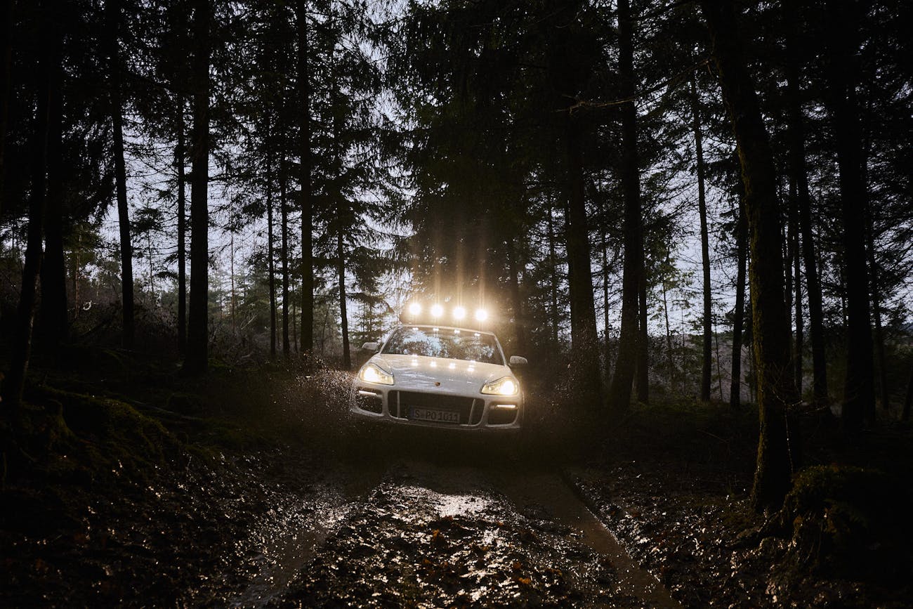 First-generation Cayenne with roof spotlights driving through dark woods