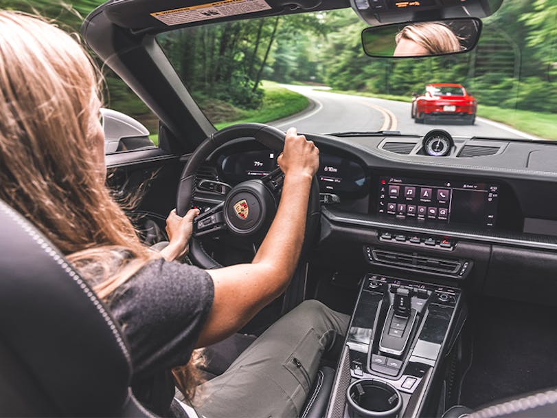 Interior of car, woman driving Porsche 911 cabriolet on road