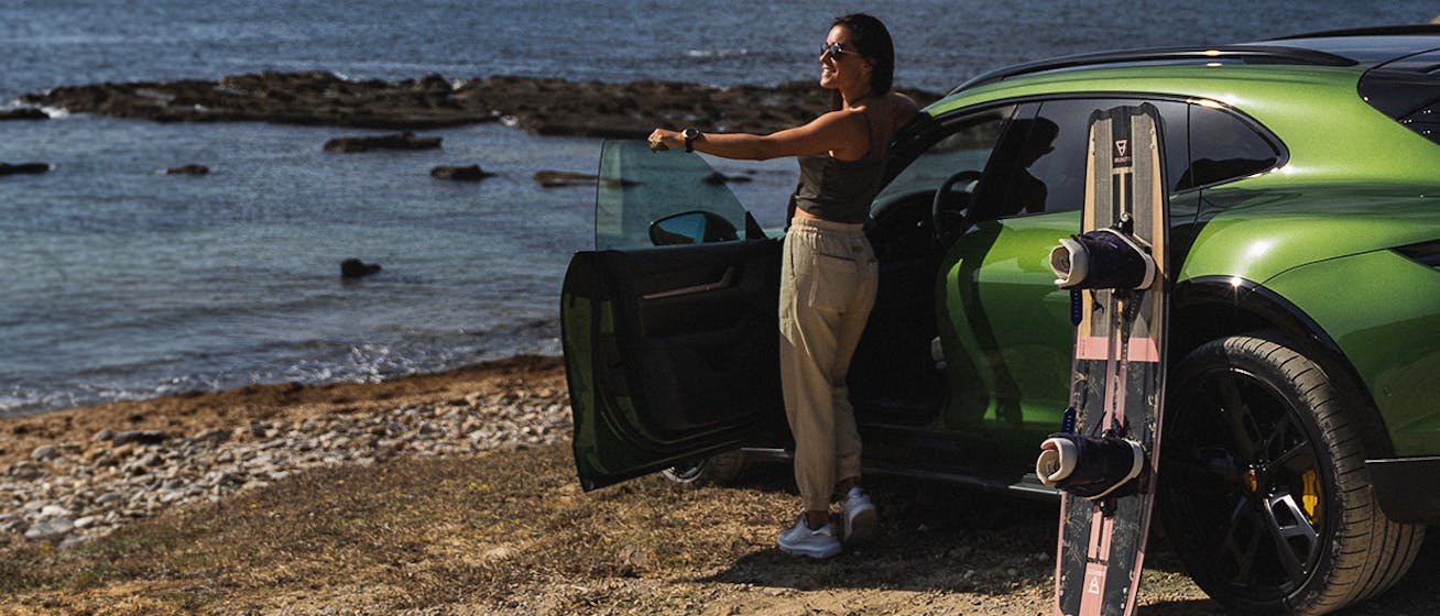 Female kitesurfer looks at ocean next Porsche Taycan Cross Turismo