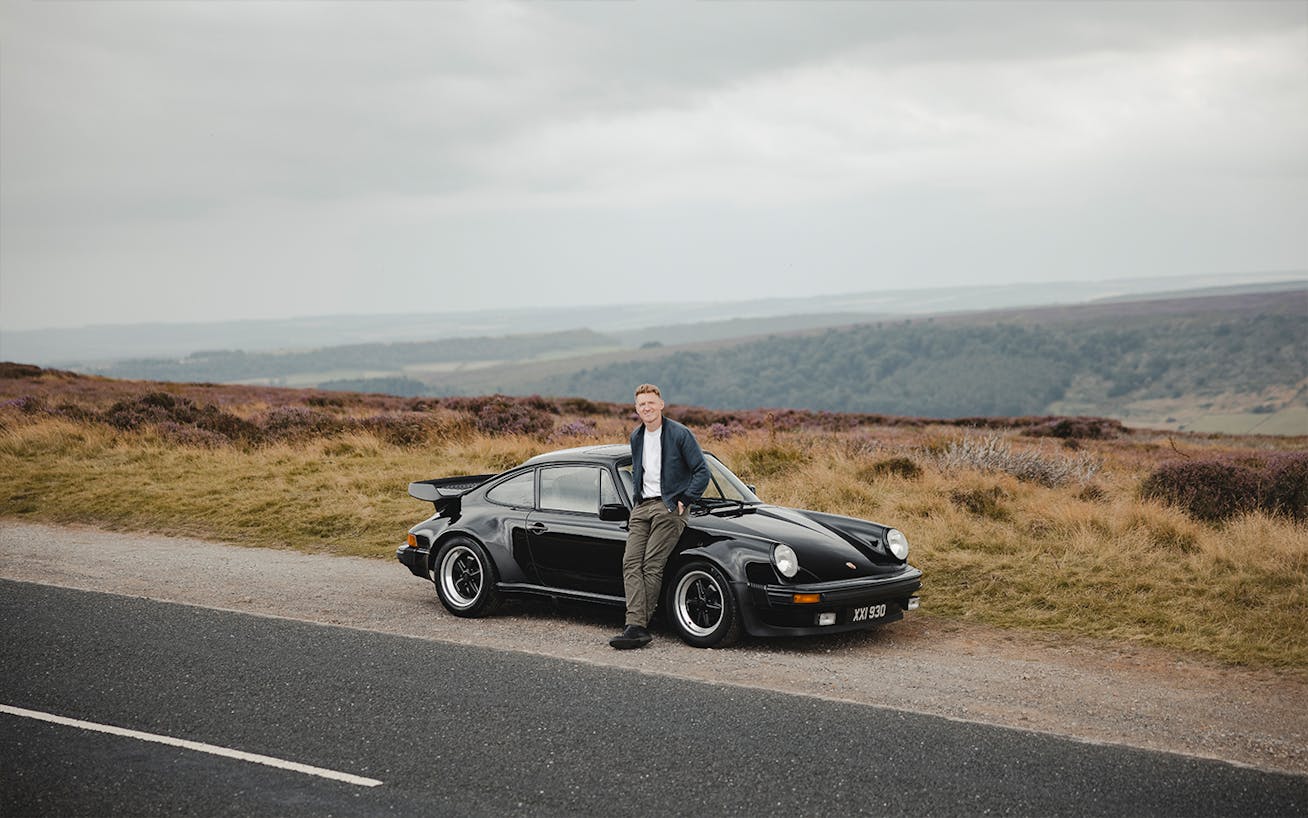 Man leaning against black 1980 Porsche 930 in nature 